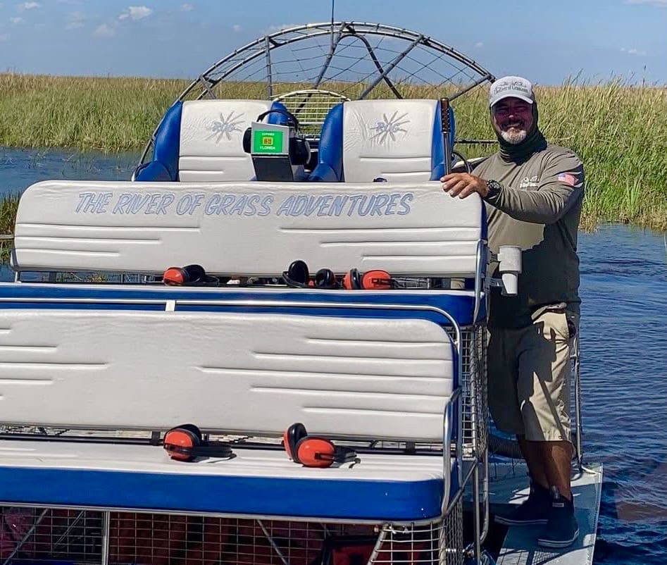 Man standing by airboat in marshland.