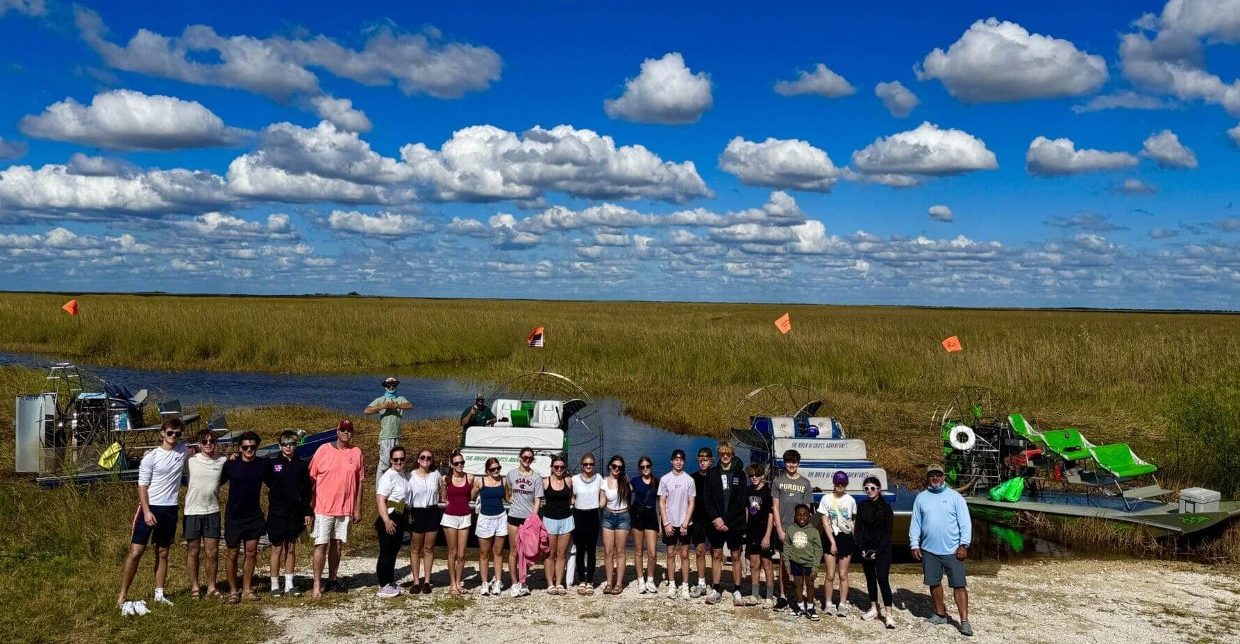 Group standing by airboats in marshland.
