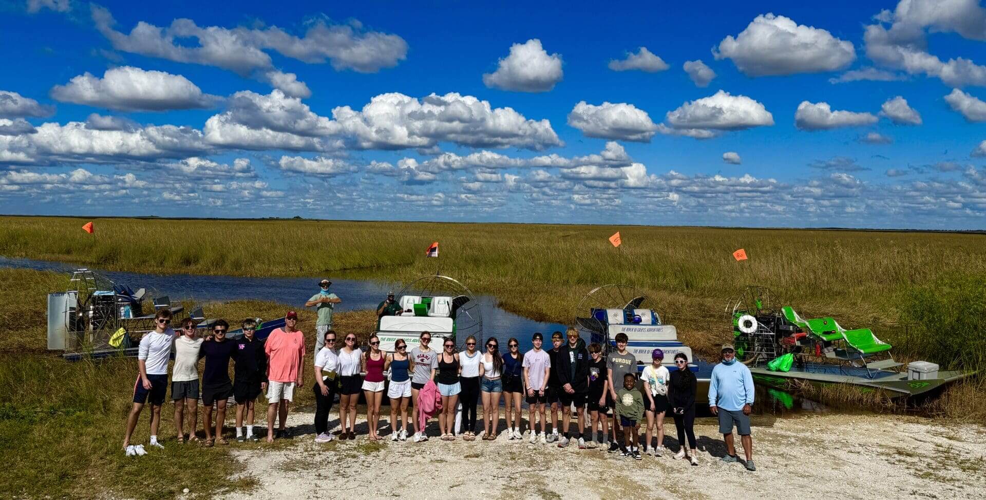 Group standing by airboats in marshland.