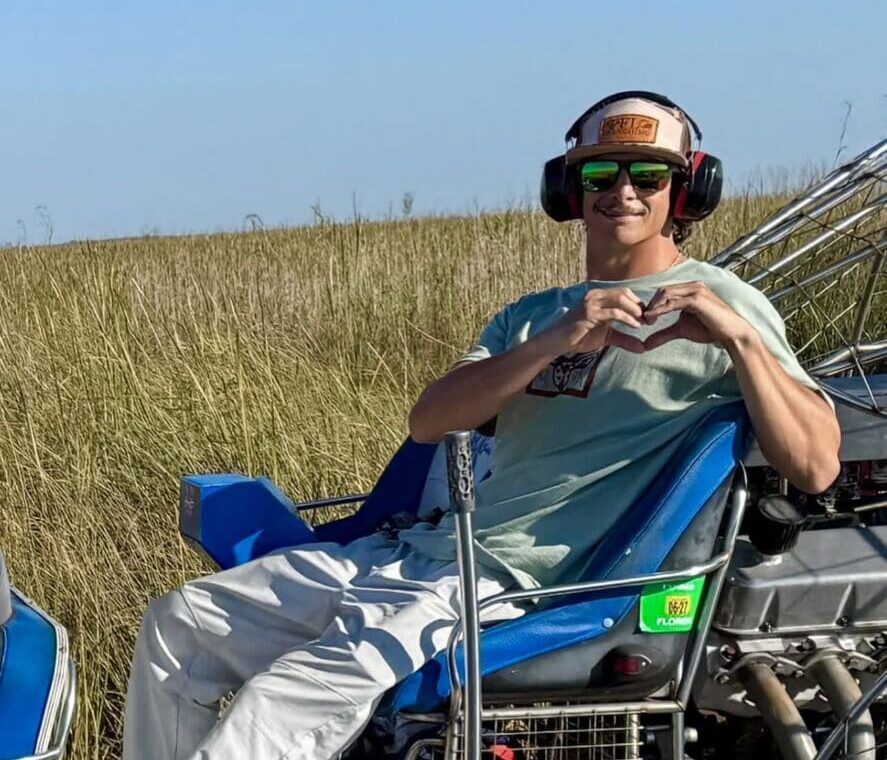 Person on airboat making heart gesture, smiling.