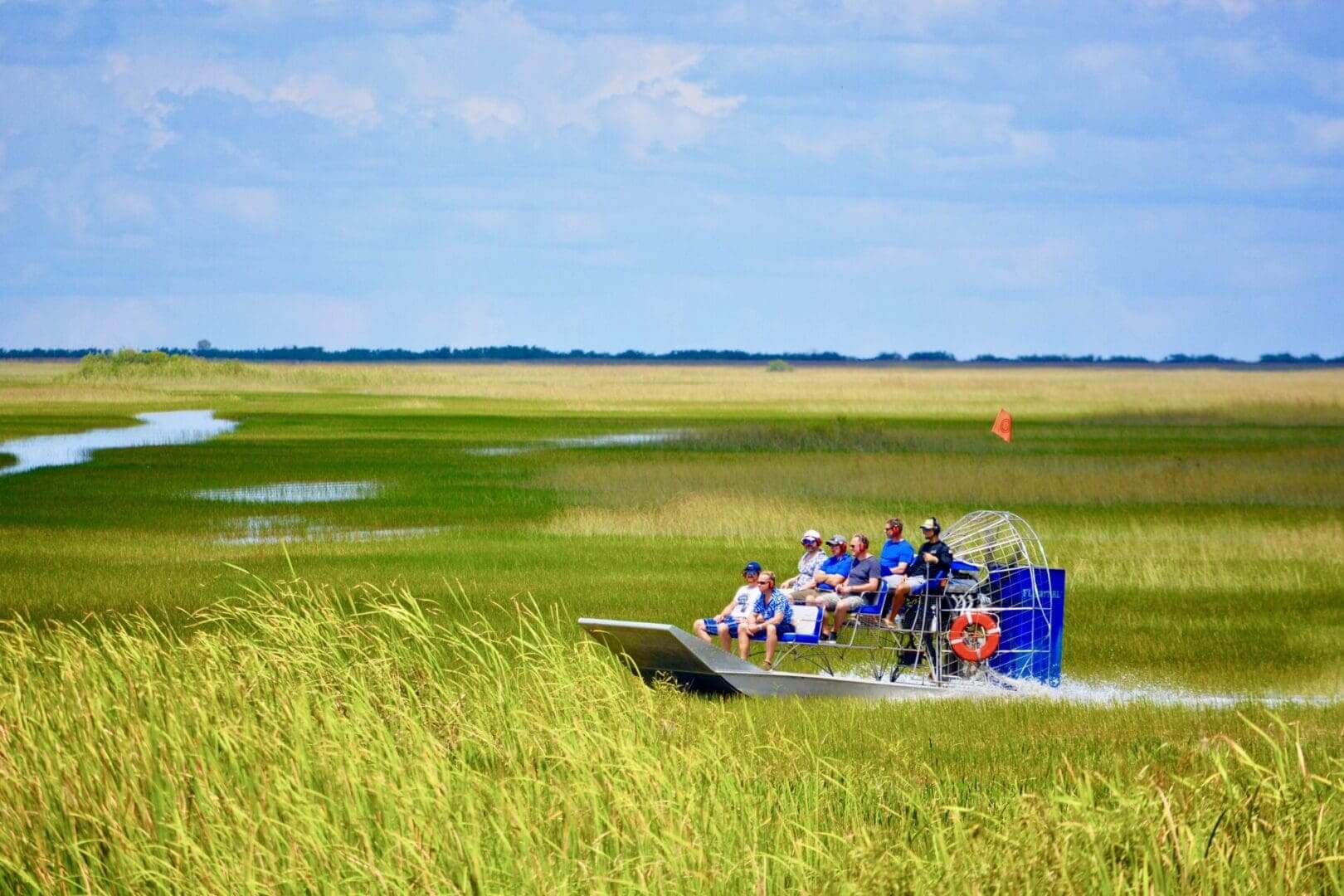 Airboat touring through grassy wetlands under sky.