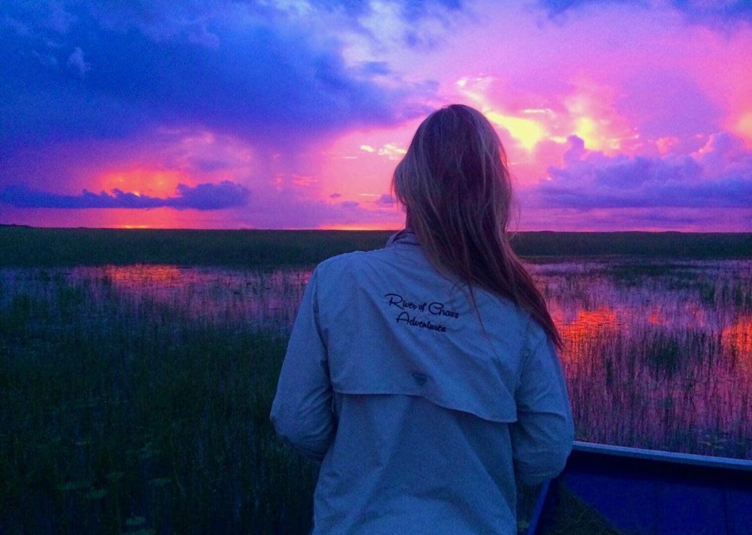 Person watching vibrant sunset over marshland.